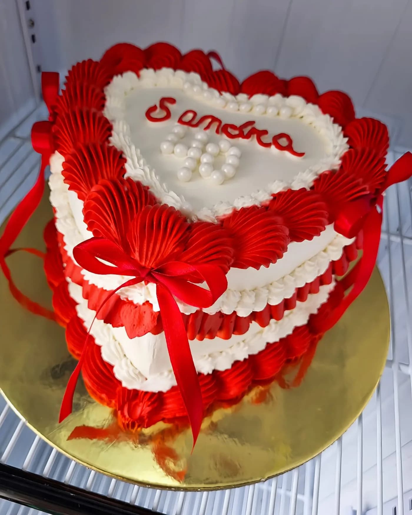Torta con forma de corazón en crema roja y blanca estilo vintage con lazo de raso